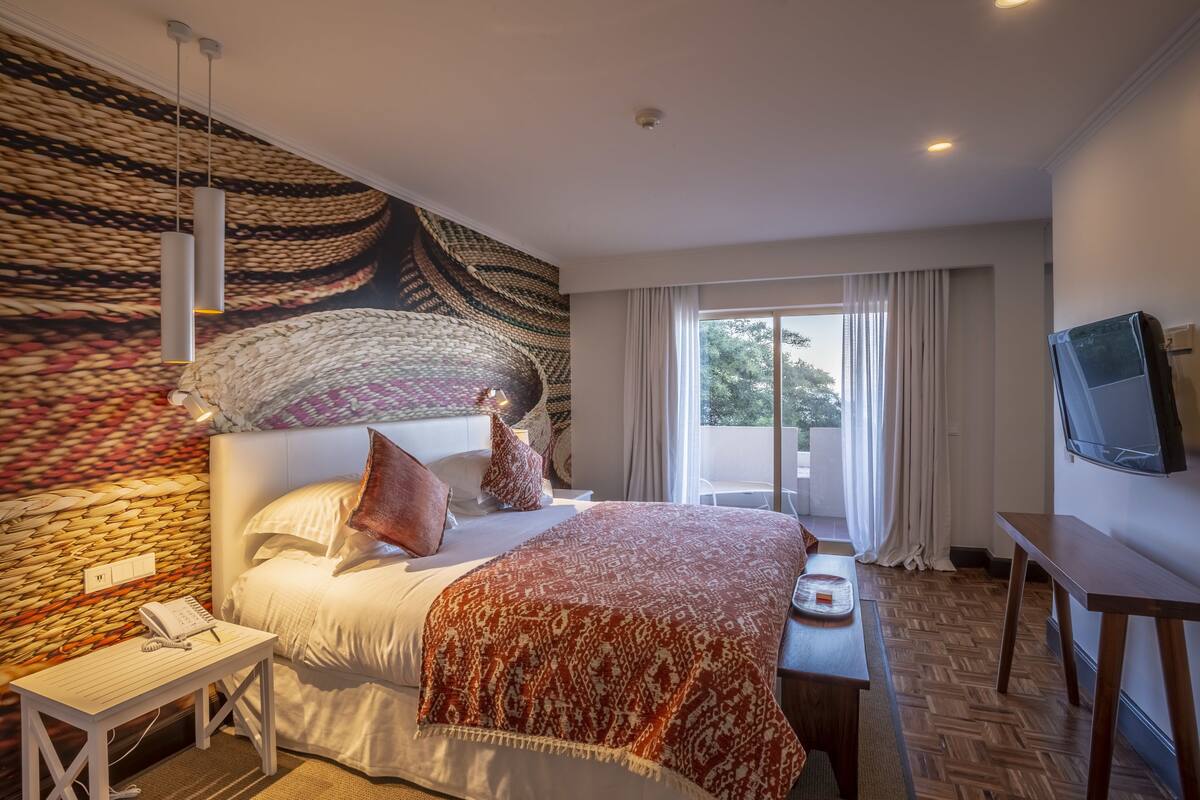 Ein Hotelzimmer mit einem großen Bett, einem Schreibtisch, einem Fernseher und Blick ins Freie.
