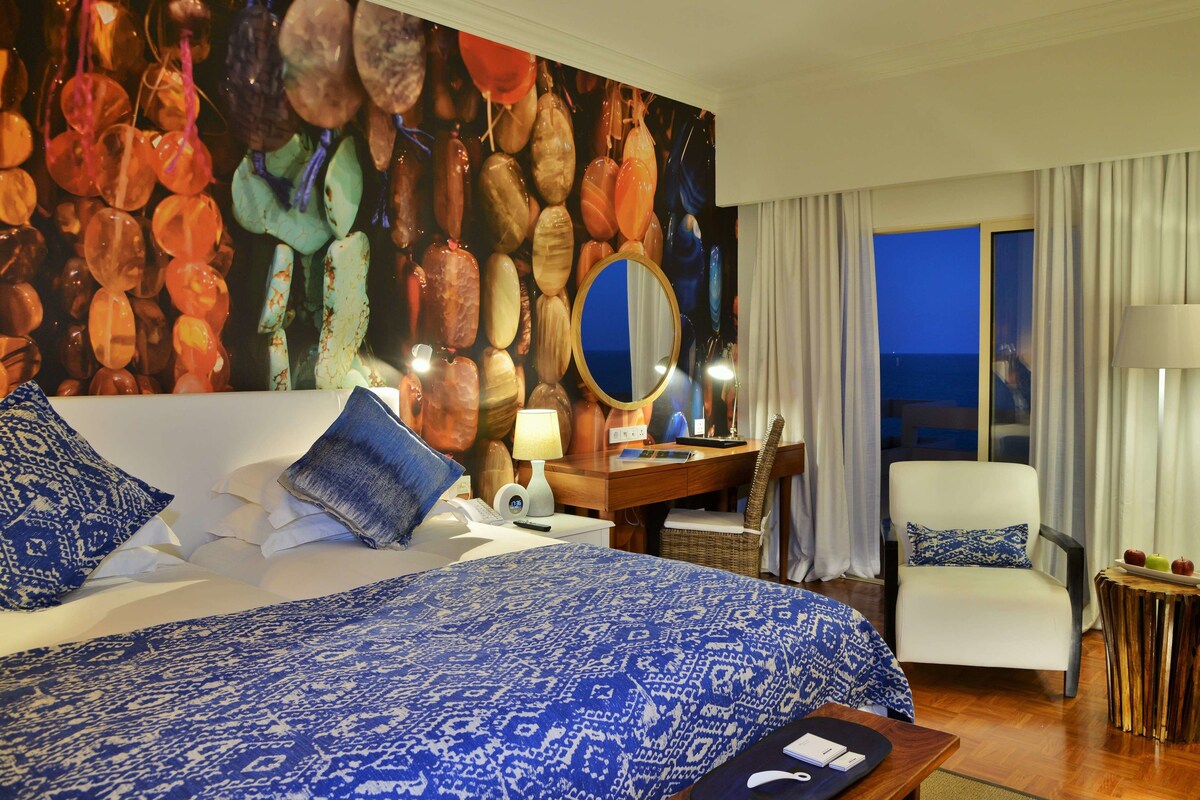 A hotel room with a large bed, a desk, a chair, and a view of the ocean.