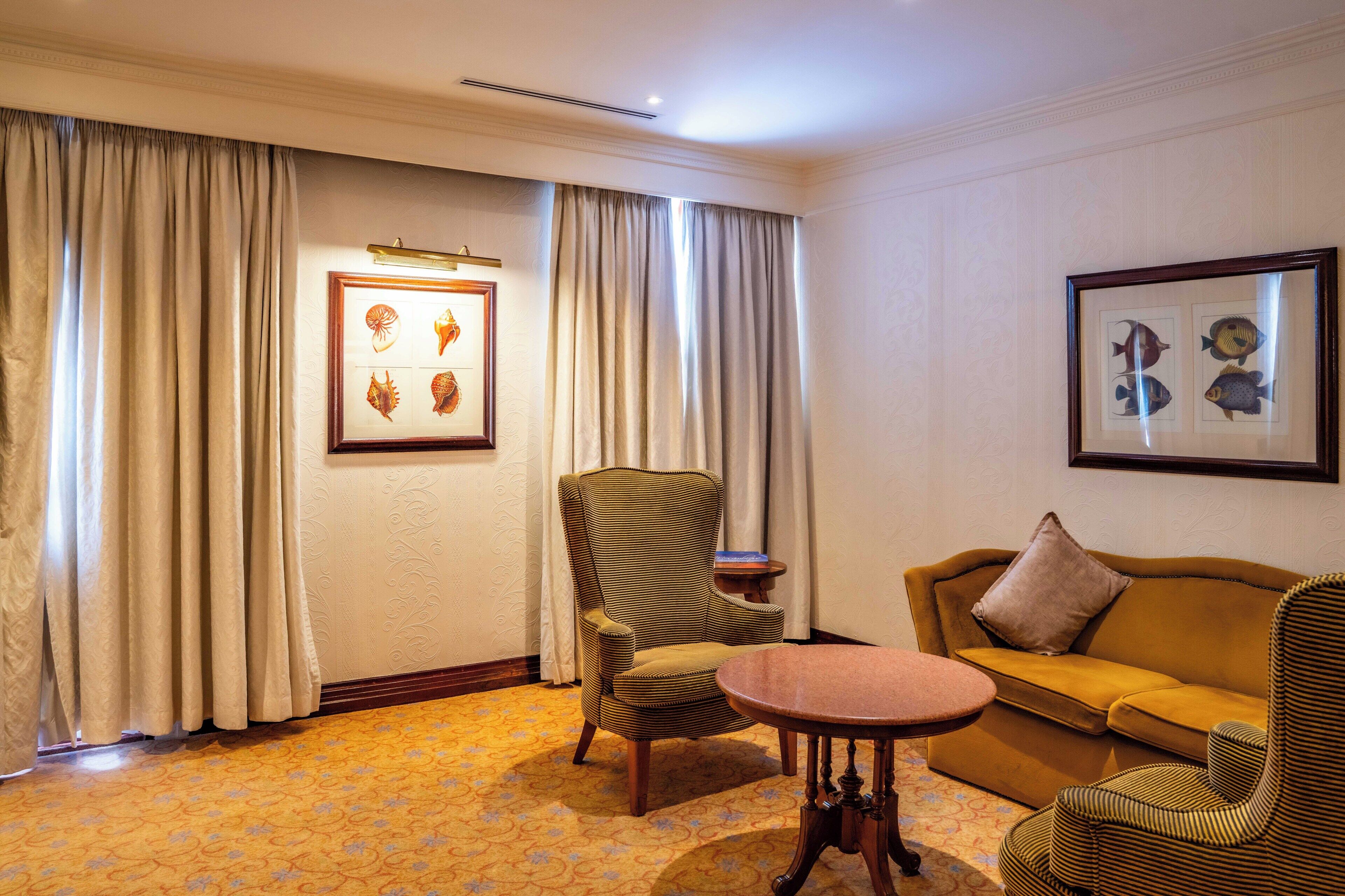 A room with a patterned carpet, a sofa, a chair, a small table, and two framed pictures on the wall.