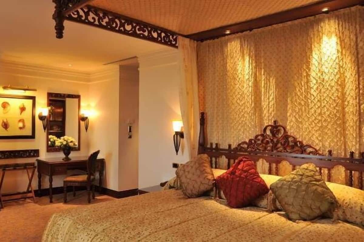 A bedroom with a large bed, a desk with a chair, a mirror, and wall sconces.