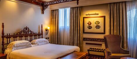 A hotel room with a large bed, a wooden headboard, a chair, a small table, and a framed picture on the wall.