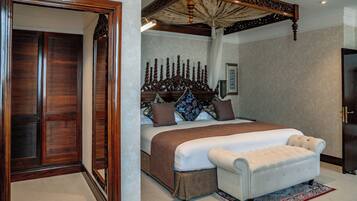 A bedroom with a large bed, a wooden headboard, a white upholstered bench, and a patterned rug.
