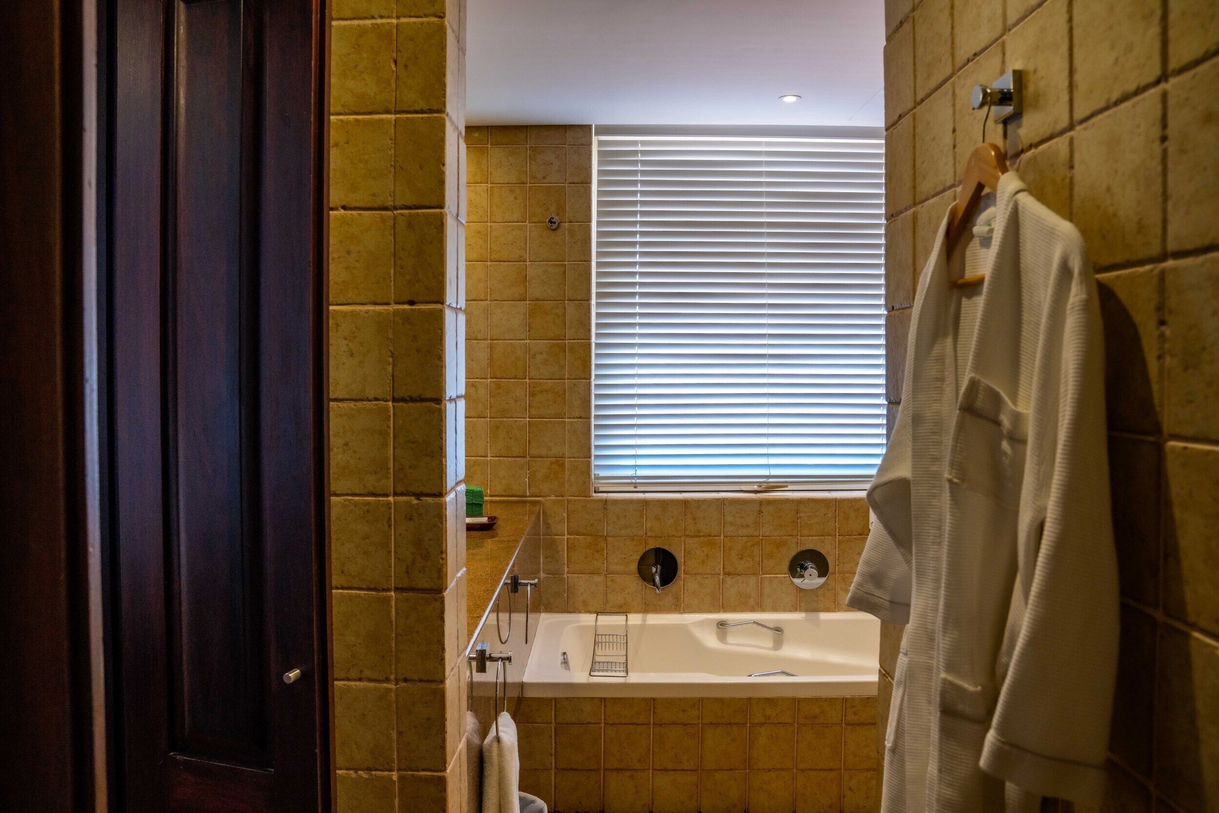 A bathroom with a bathtub, a towel rack, and a window with blinds.