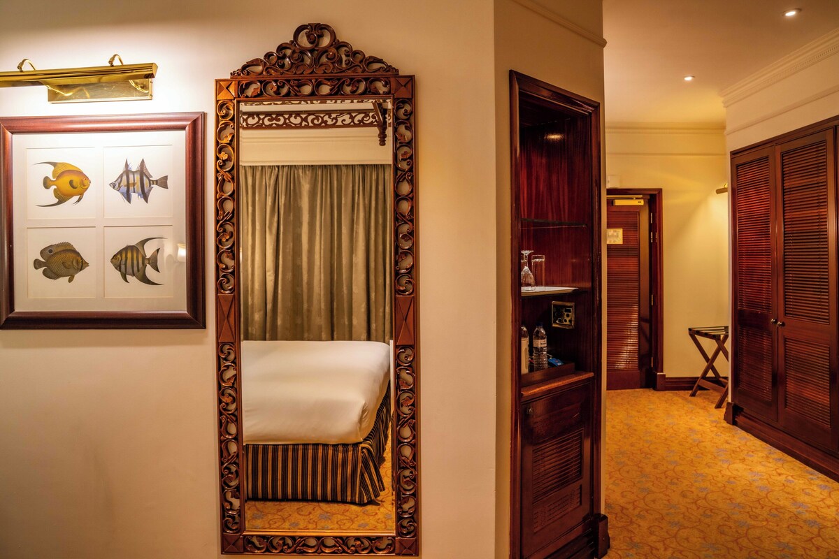 A hotel room with a large mirror, a bed, a framed fish artwork, a wooden wardrobe, and a small table with toiletries.