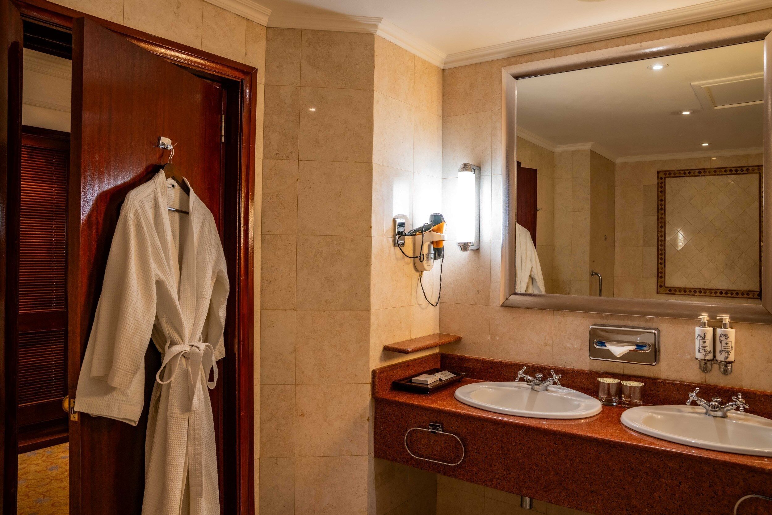 A hotel bathroom with two sinks, a robe rack, a towel dispenser, and a large mirror.