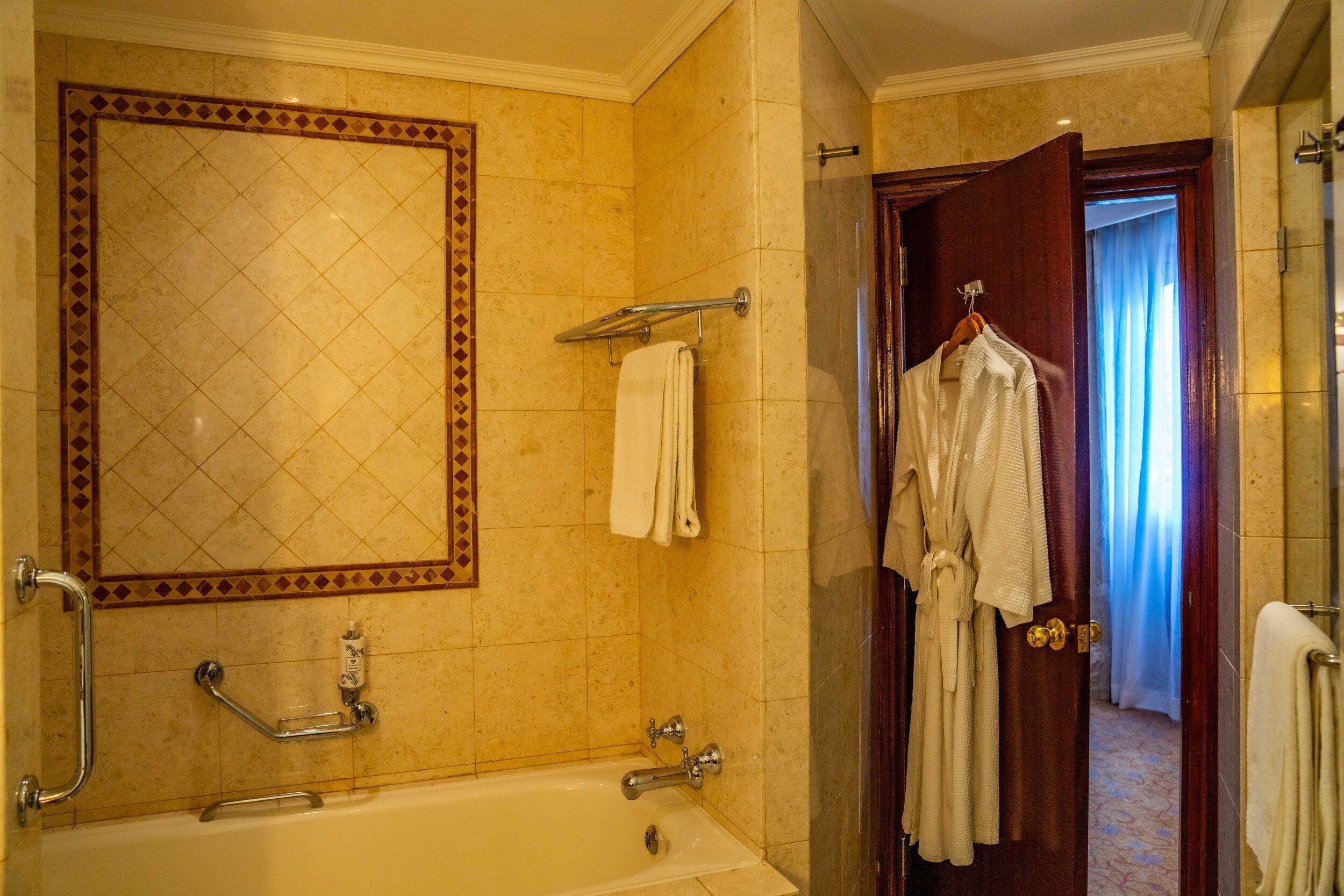 Un baño con bañera, perchero, una bata colgada en la puerta y zona de ducha.