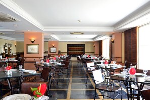 A spacious restaurant with multiple tables and chairs, a patterned floor, and framed artwork on the walls.