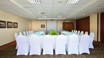 Un salón de conferencias con una larga mesa, sillas blancas y botellas de agua.