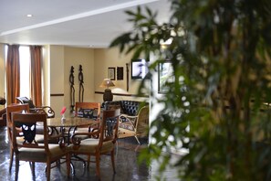 A dining area with a round table, chairs, a sofa, and a television mounted on the wall. - Pestana Rovuma (Maputo)