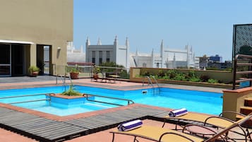 Piscina no terraço com espreguiçadeiras e vista para o horizonte da cidade.