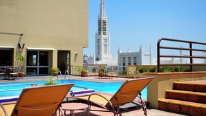 A rooftop pool area with lounge chairs, a view of a church spire, and a building with a cross on top. - Pestana Rovuma (Maputo)