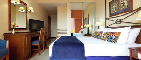 A hotel room with a bed, a desk, a chair, a television, and a mirror.