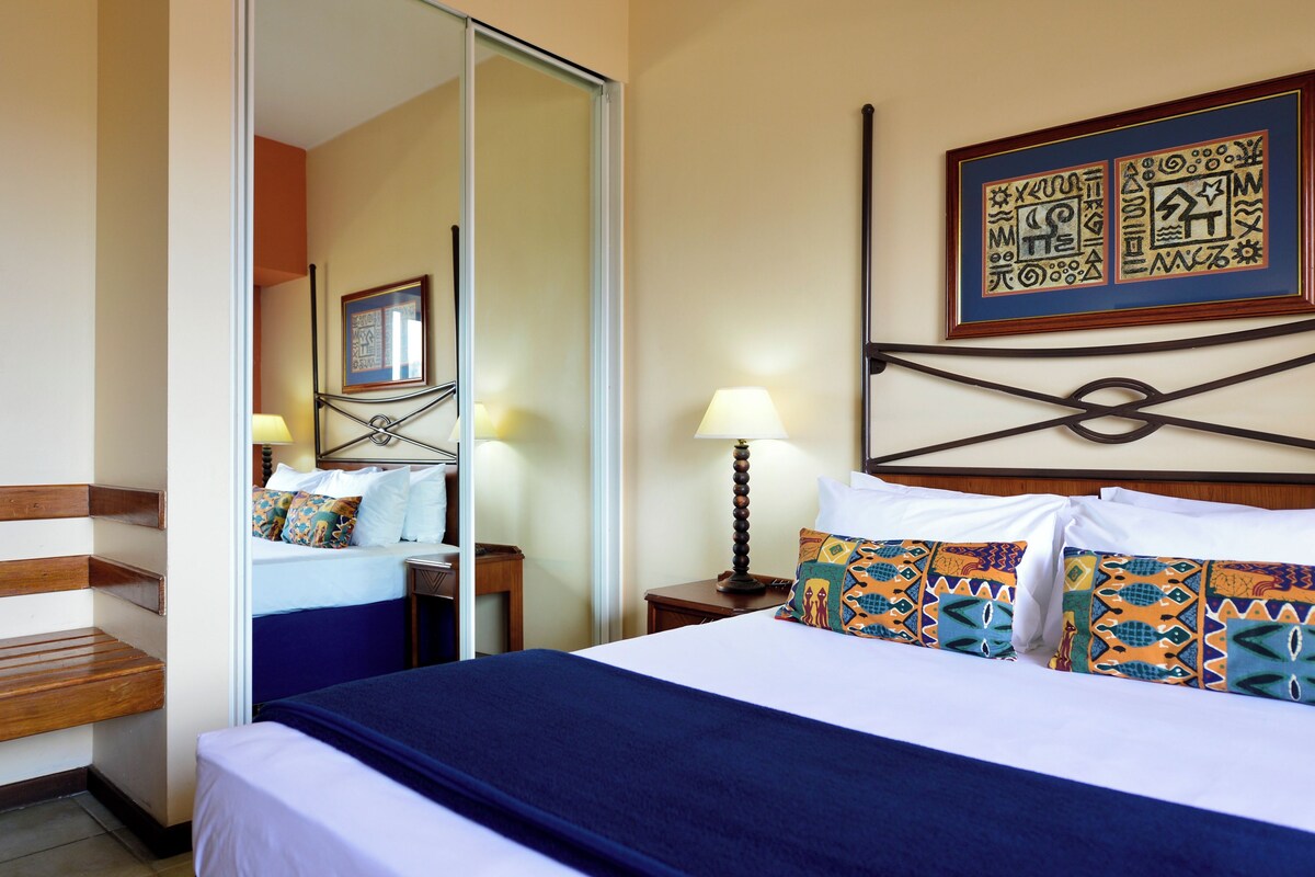 Una habitación de hotel con una cama, una mesita de noche, una lámpara, un espejo y un cuadro colgado en la pared.
