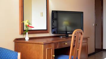 Una habitación de hotel con un escritorio de madera, un televisor, una silla y un sofá azul.