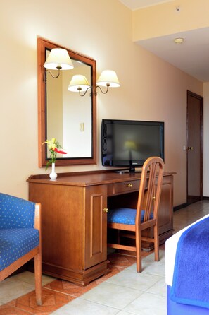 A hotel room with a wooden desk, a television, a chair, and a blue sofa. - Pestana Rovuma (Maputo)