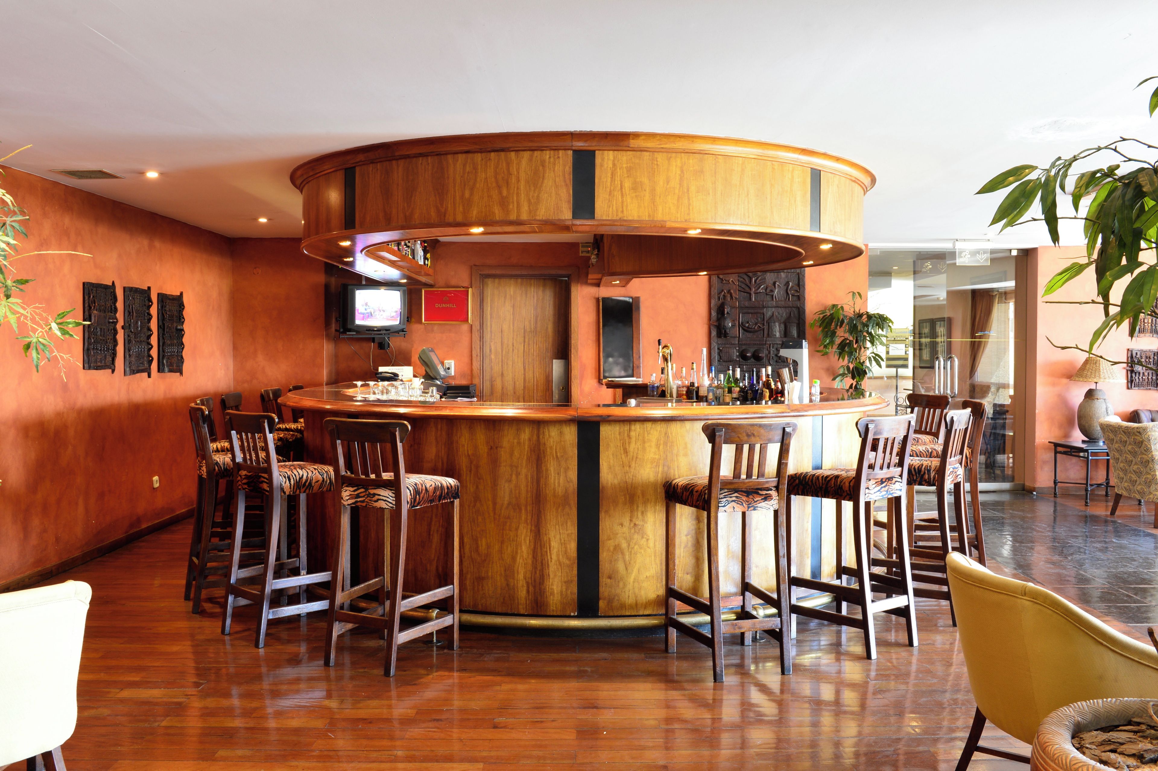 Zona de bar con un mostrador de madera curvada, taburetes y un televisor montado en la pared.