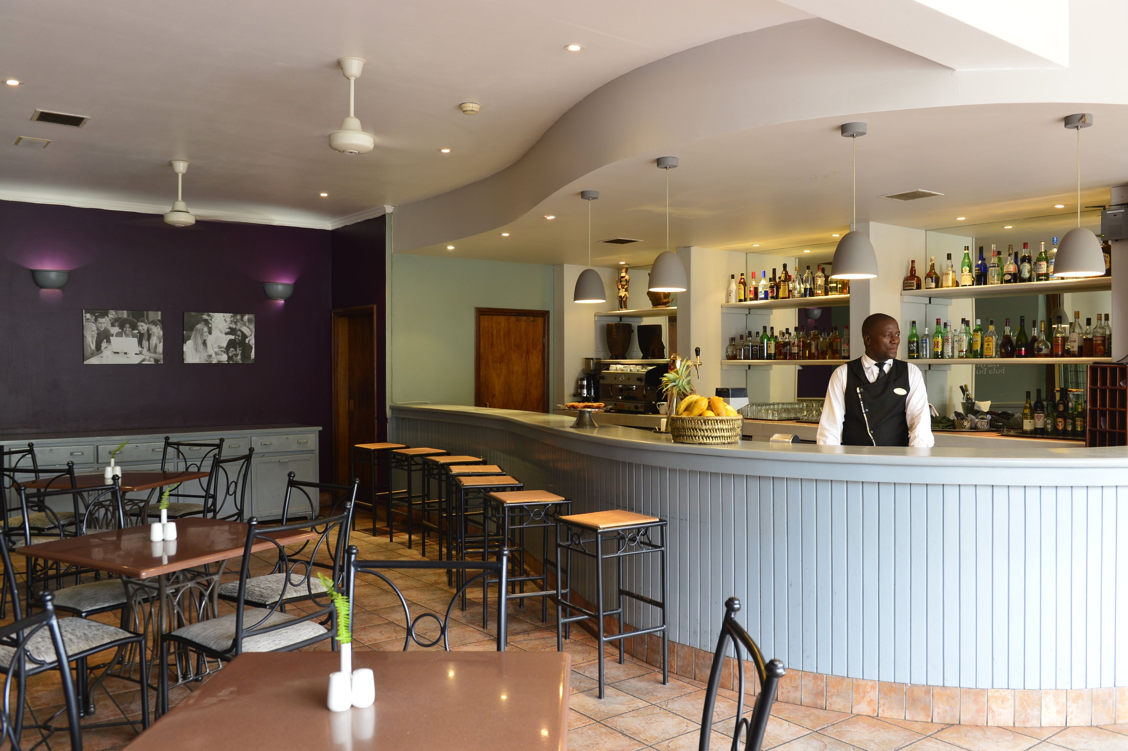 Interior de un restaurante con barra, asientos y un cantinero.