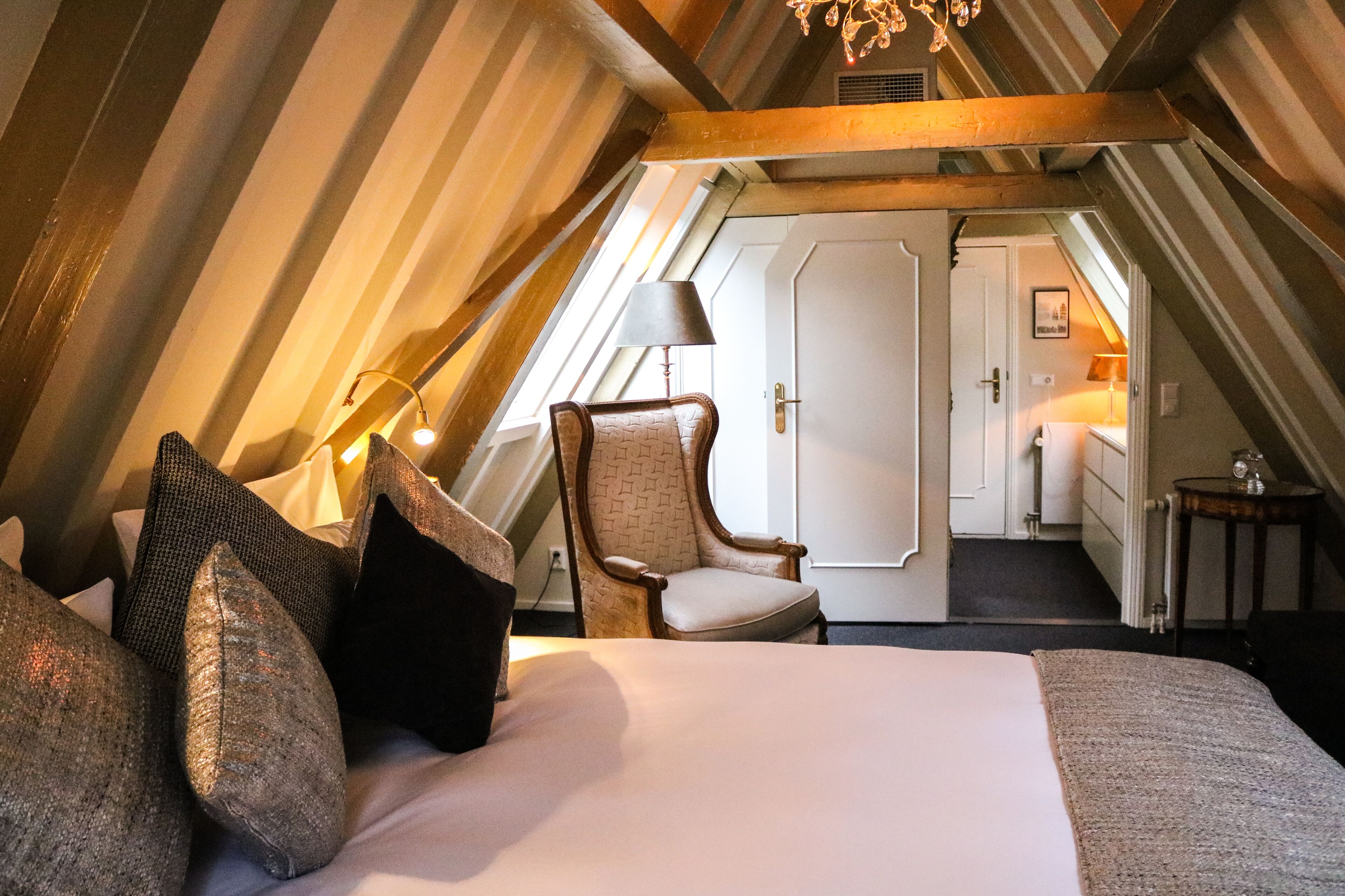 Ein gemütliches Schlafzimmer im Dachgeschoss mit einem großen Bett, einem Holzstuhl und einer Lampe.
