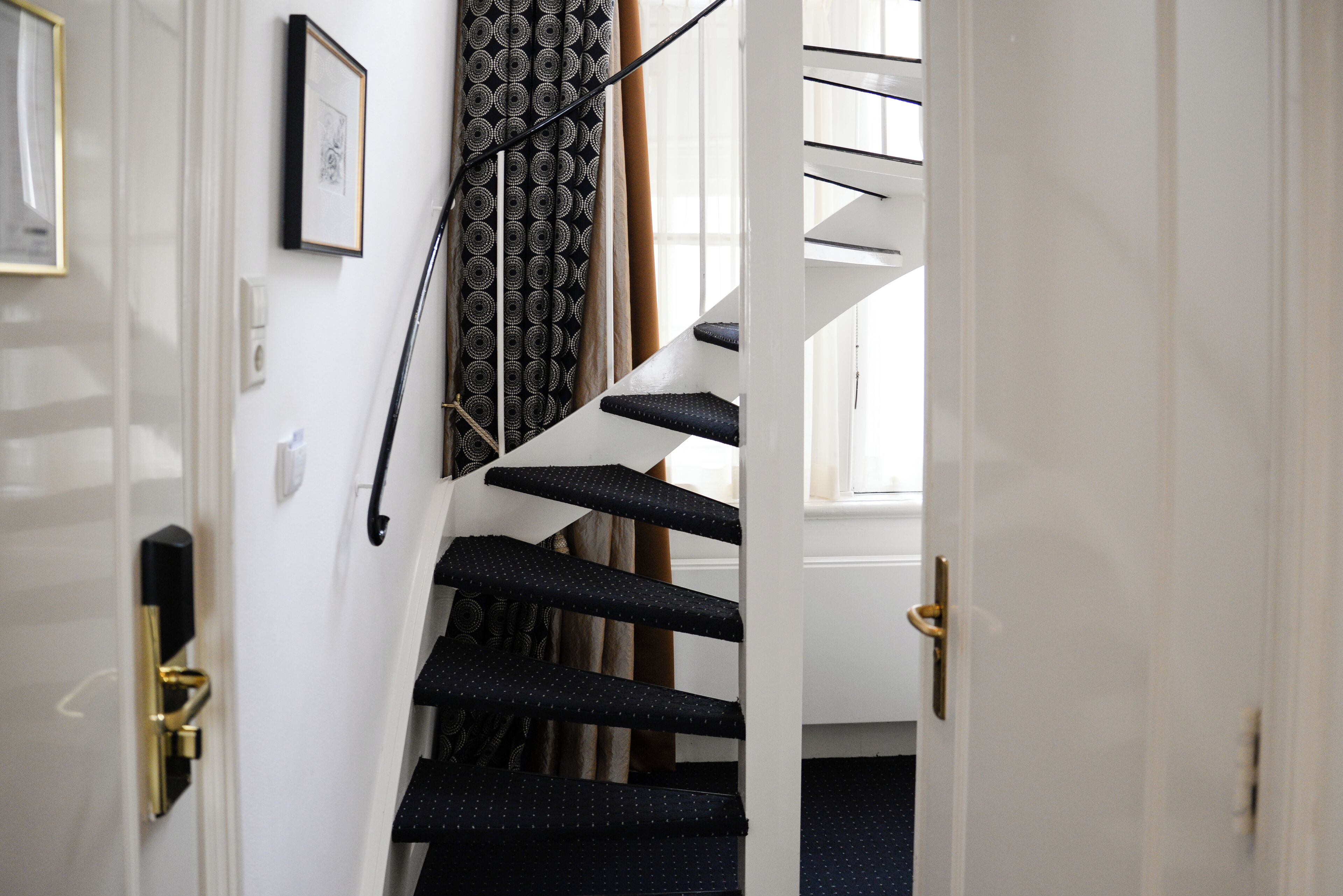 Un escalier recouvert d’une moquette à motifs, avec une main courante et une porte dotée d’une poignée en laiton.