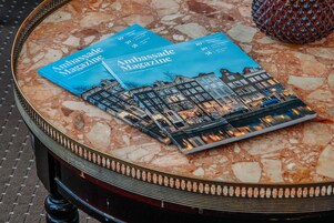 Une table sur laquelle reposent deux magazines intitulés « Ambassadge Magazine », le tout sur une surface en marbre.