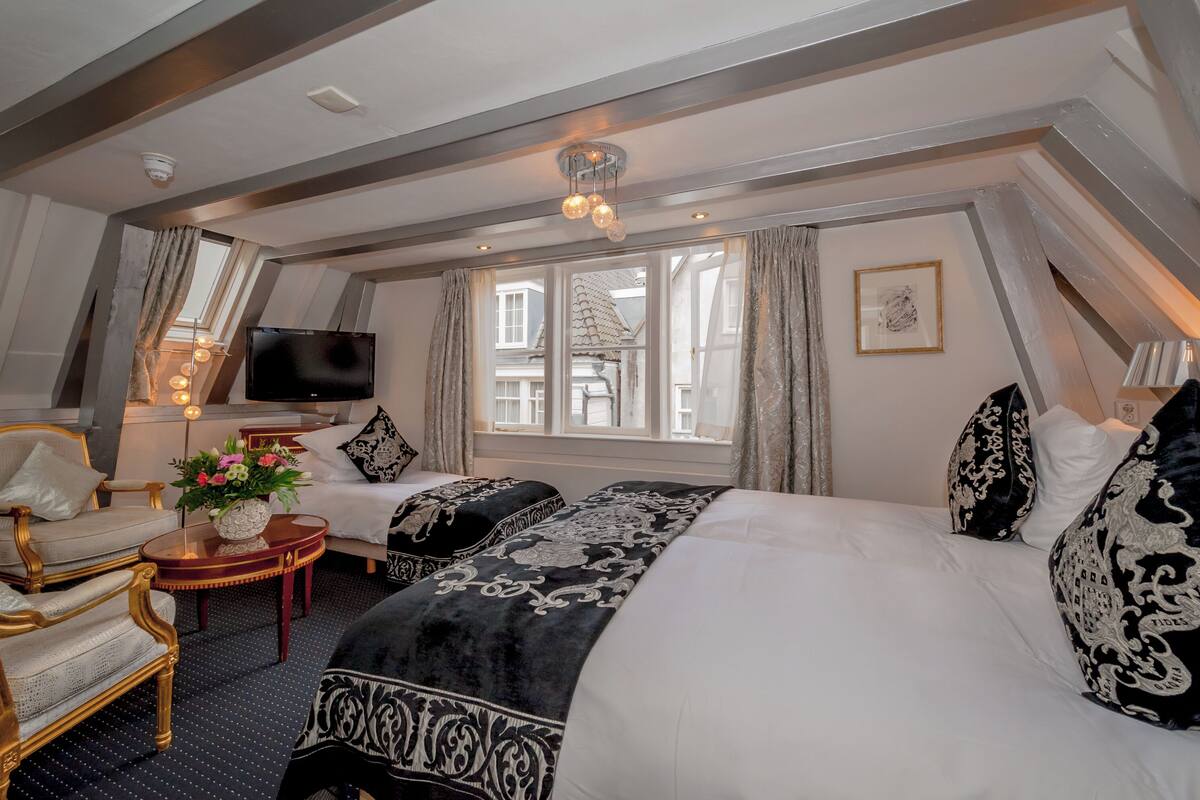 Quarto de hotel com uma cama grande, televisão, uma mesinha com flores e vista para o exterior.