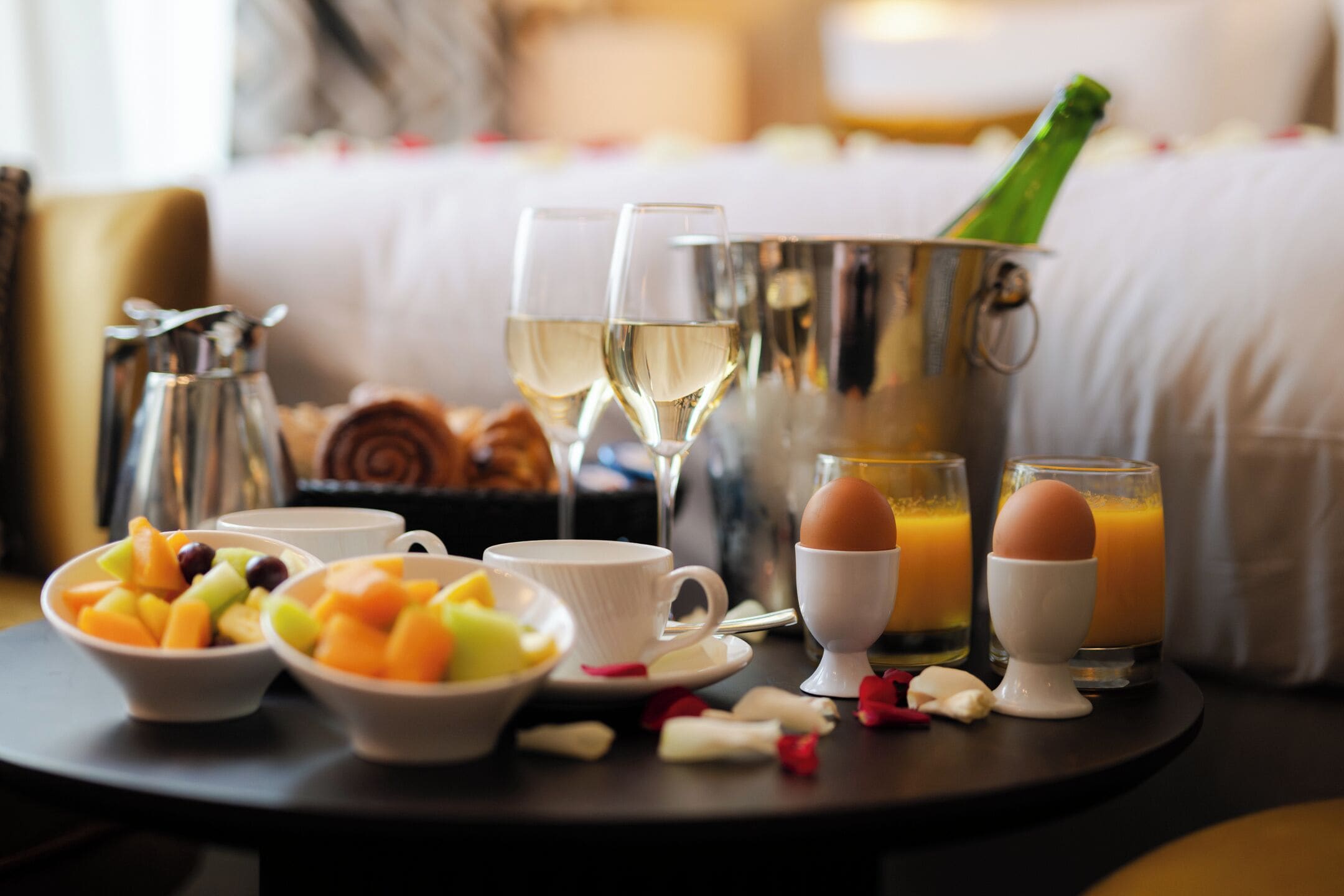 Un desayuno con fruteros, huevos, jugo y copas de champán sobre una bandeja.