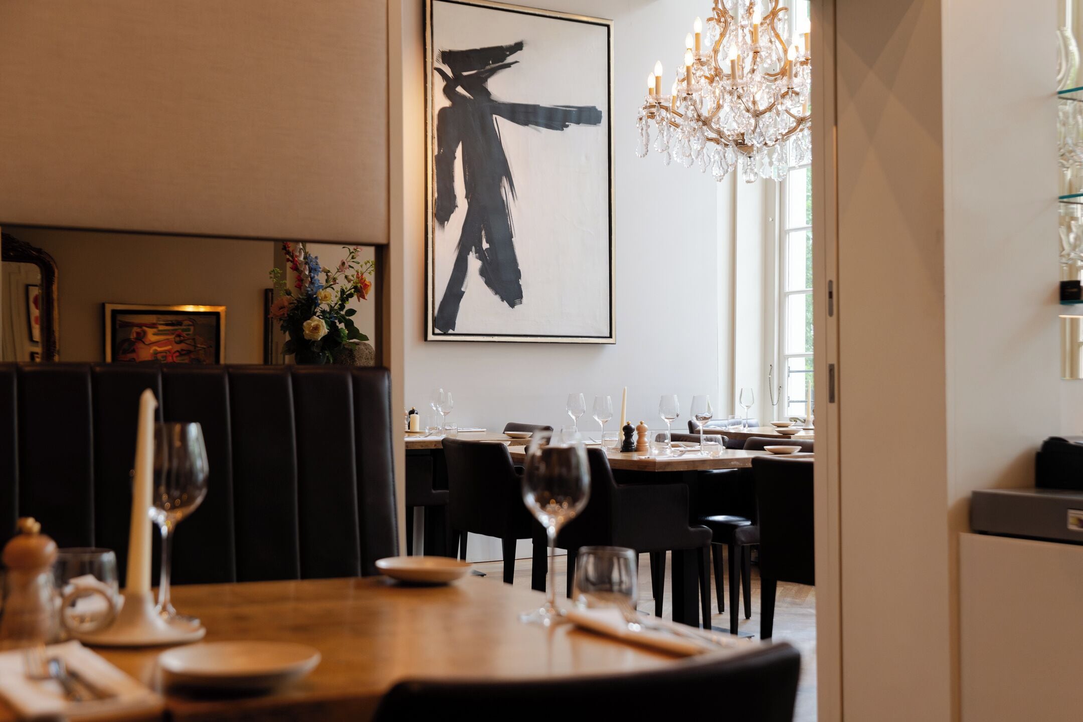 A dining area with a wooden table set for two, a chandelier, and a large abstract painting on the wall.