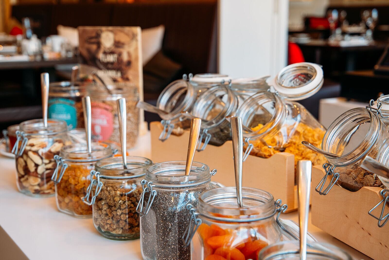 Una mesa de buffet con diversos alimentos en frascos de vidrio con cierres metálicos y cucharas.