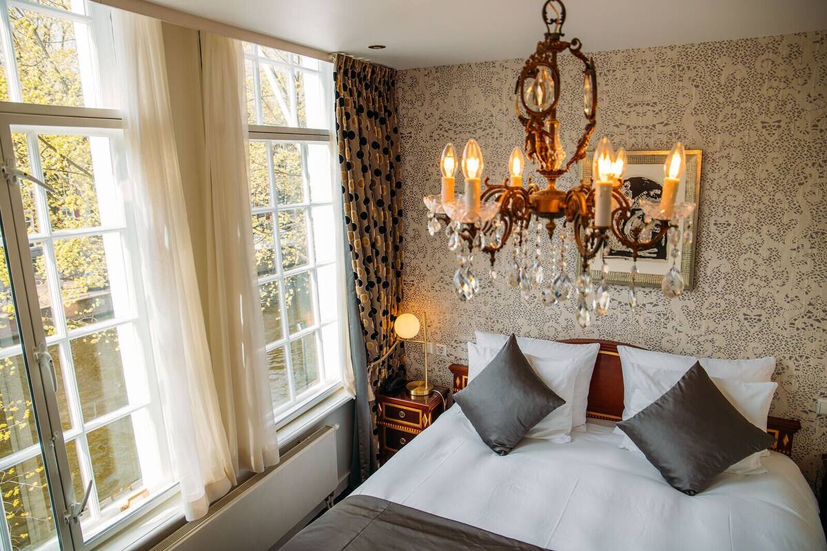 Quarto com cama grande, lustre, mesa de cabeceira e janela com cortinas.