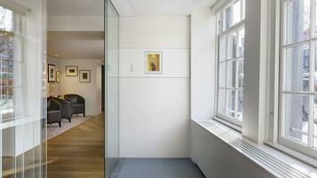 Un pasillo con un panel de vidrio, una obra de arte enmarcada en la pared y una zona de estar con sillones.