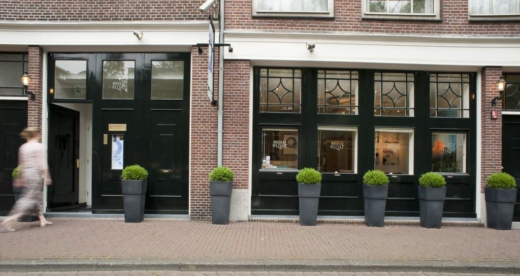 A brick building with black doors and windows, potted plants, and a pedestrian walkway.