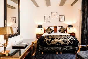 Ein Hotelzimmer mit einem großen Bett, zwei Nachttischen, einem Schreibtisch mit Lampe und einem Sessel.