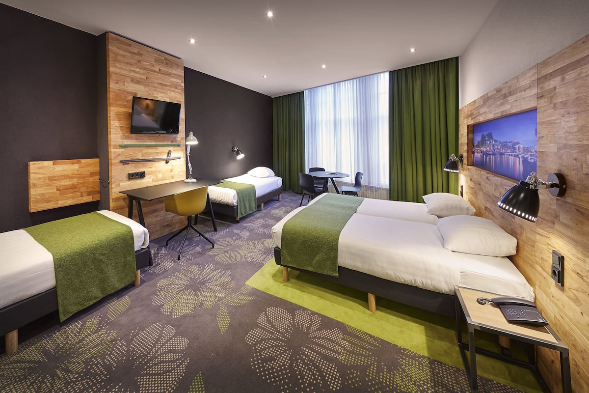 A hotel room with two beds, a desk, a chair, a TV, and a cityscape painting.