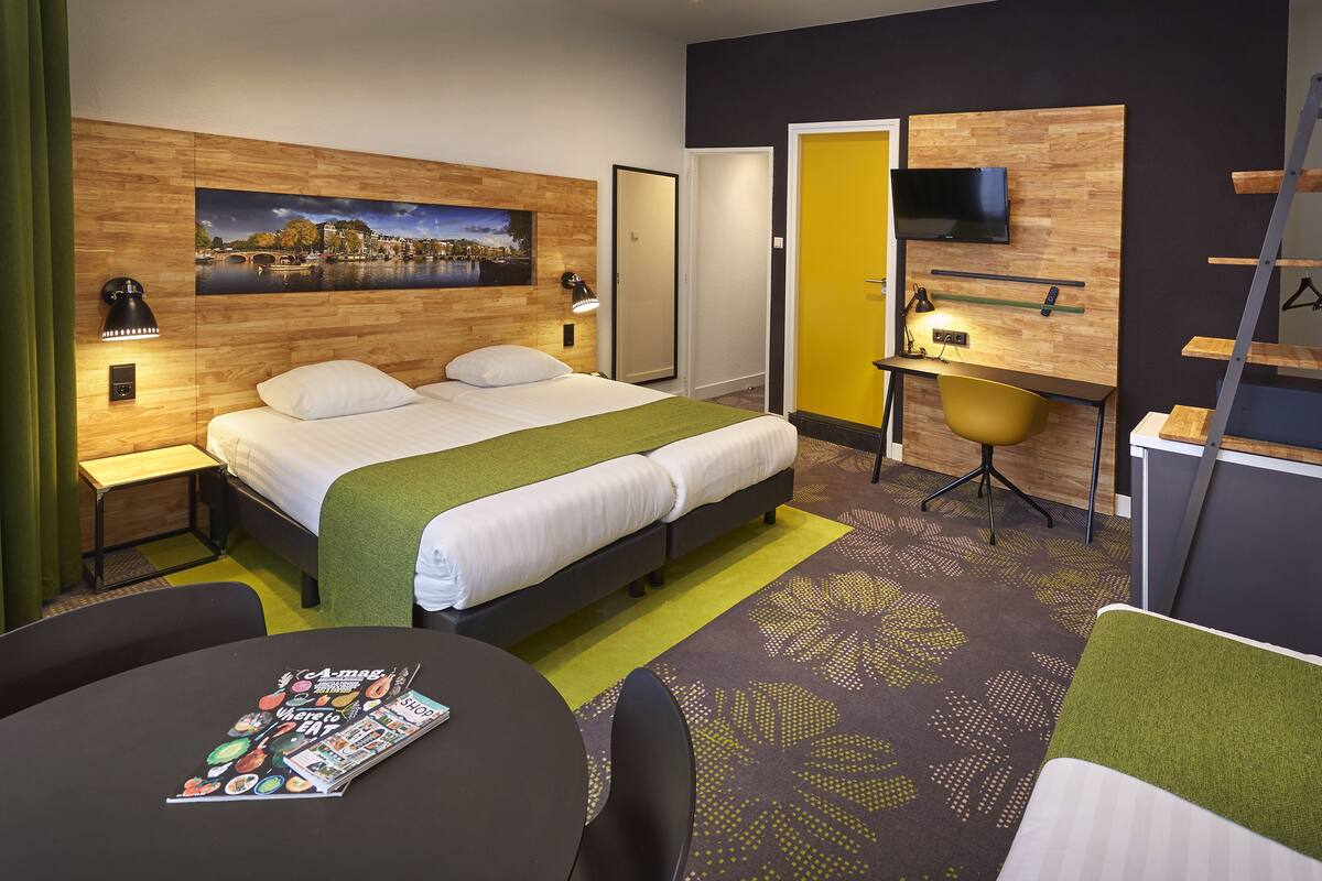 A hotel room with a bed, bedside tables, a desk with a chair, a TV, and a painting on the wall.