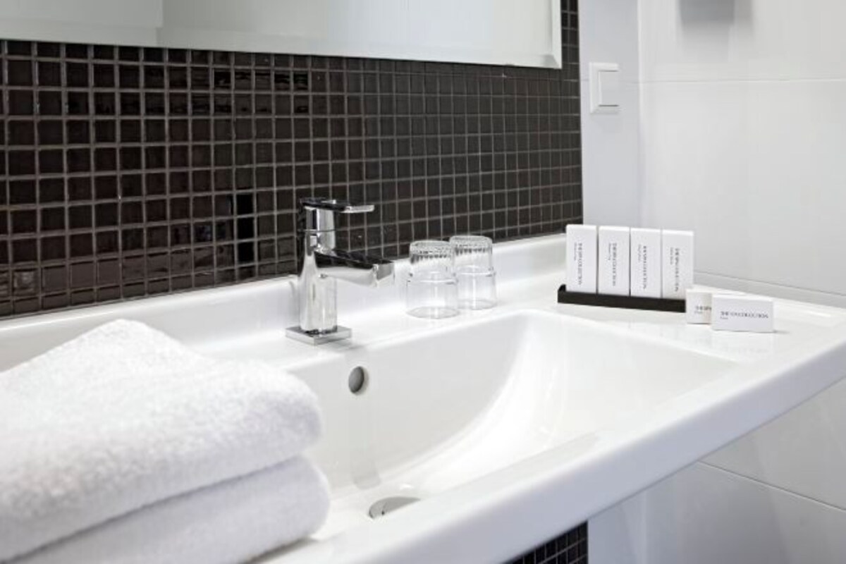 A white bathroom sink with a black tiled backsplash, a white towel, and a bottle of hand soap.