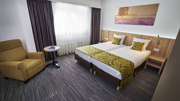 Een hotelkamer met een bed, een stoel, een nachtkastje, een lamp en een schilderij aan de muur.