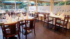 Een restaurant met ronde tafels, houten stoelen en uitzicht op de omgeving.