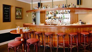 Een bar met houten krukken, een toog en diverse flessen en glazen.
