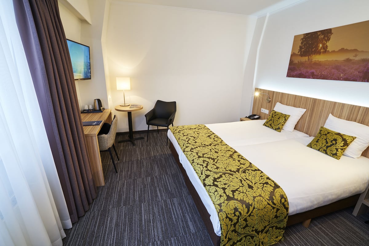 Een hotelkamer met een groot bed, een bureau, een stoel, een televisie en een schilderij aan de muur.