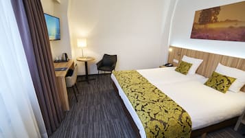 A hotel room with a large bed, a desk, a chair, a TV, and a painting on the wall.