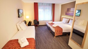 Hotelkamer met twee bedden, een bureau met lamp, een stoel, een televisie en een raam met gordijnen.