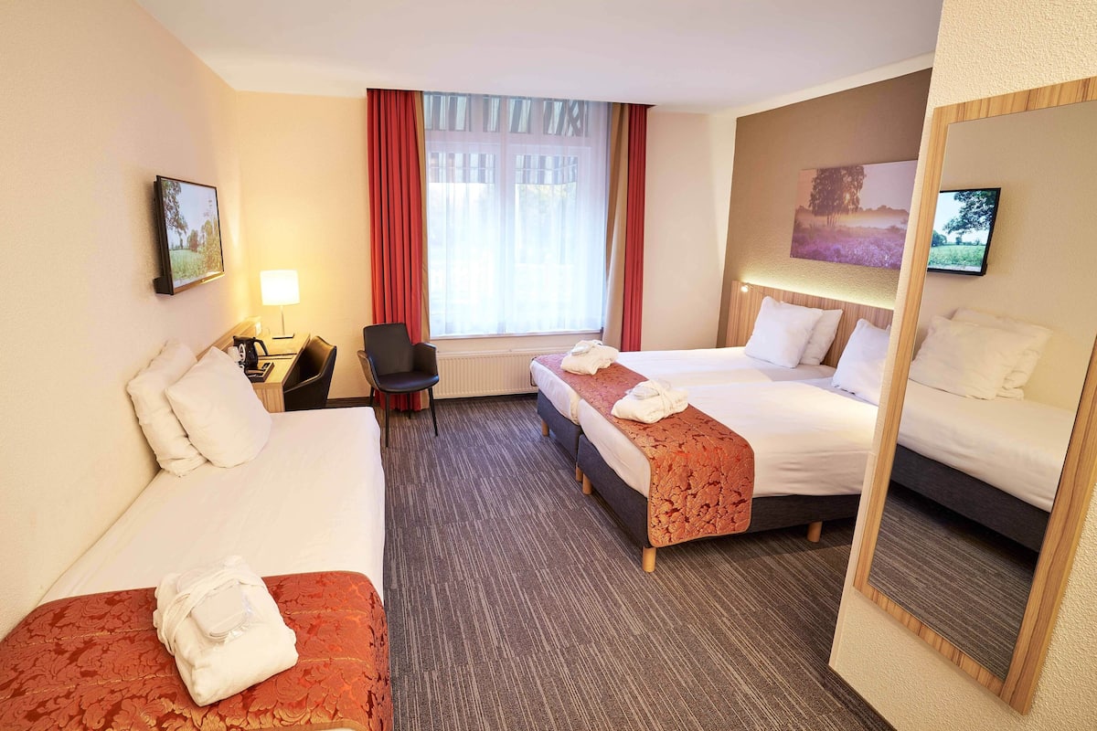 Hotelkamer met twee bedden, een bureau met lamp, een stoel, een televisie en een raam met gordijnen.