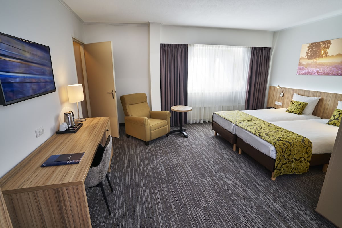Een hotelkamer met een bed, een bureau, een stoel, een klein tafeltje en een televisie.