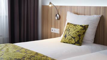 Una habitación de hotel con una cama bien hecha, una lámpara de noche y un ventanal con cortinas.
