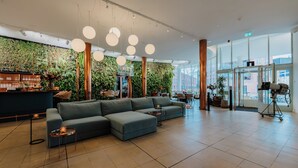 A modern lobby with a green wall, a sectional sofa, and a bar area. - Gooiland Hotel (Hilversum)