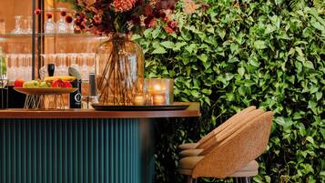 A bar area with a wooden counter, a vase with flowers, a plate of fruit, and a chair.