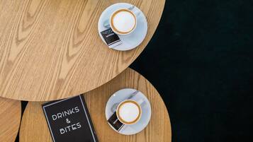 A round wooden table with two white cups of coffee and a menu titled "Drinks & Bites".