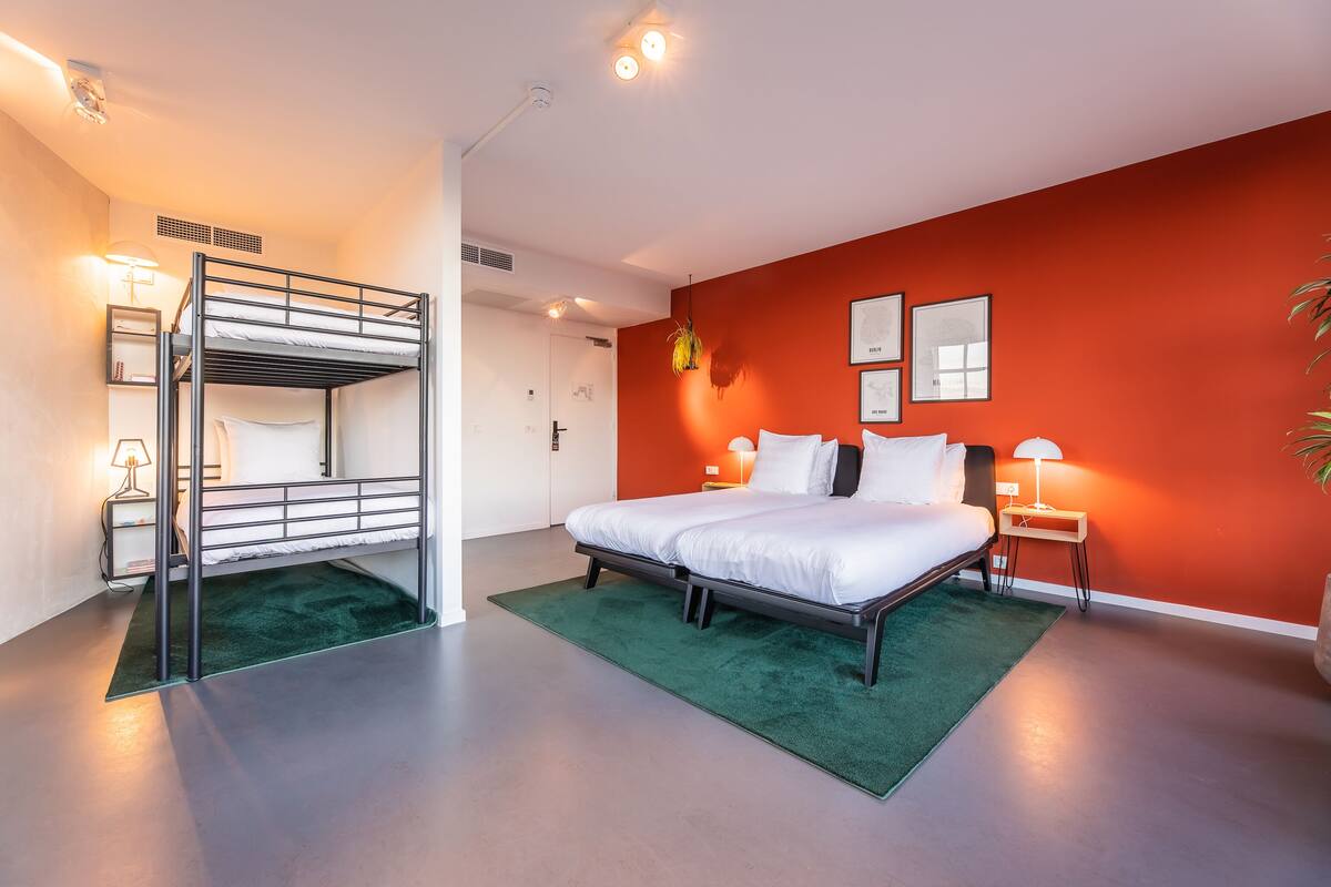 A modern hotel room with a bunk bed, a large bed, and a green rug.
