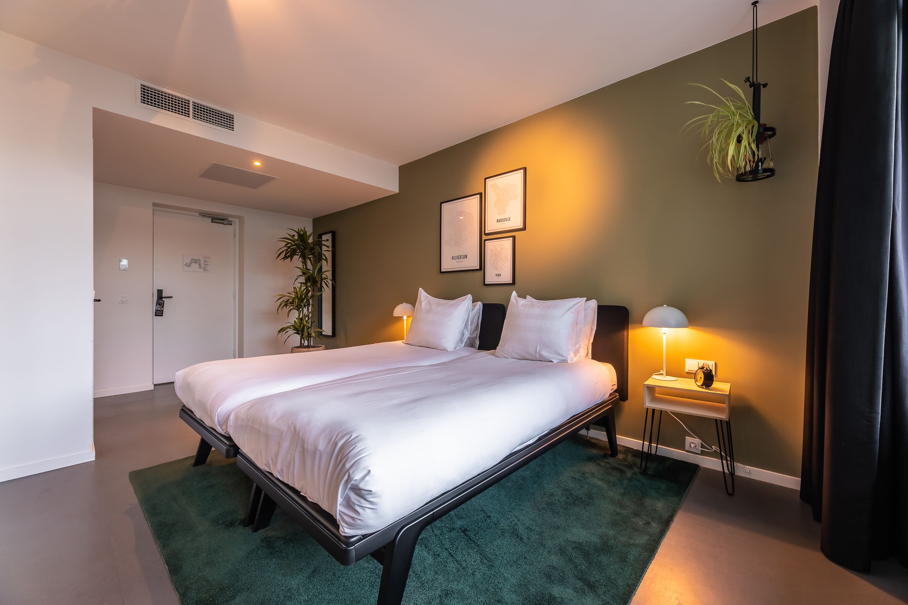 A neatly made bed with white linens, a bedside table with a lamp, and a framed map on the wall.