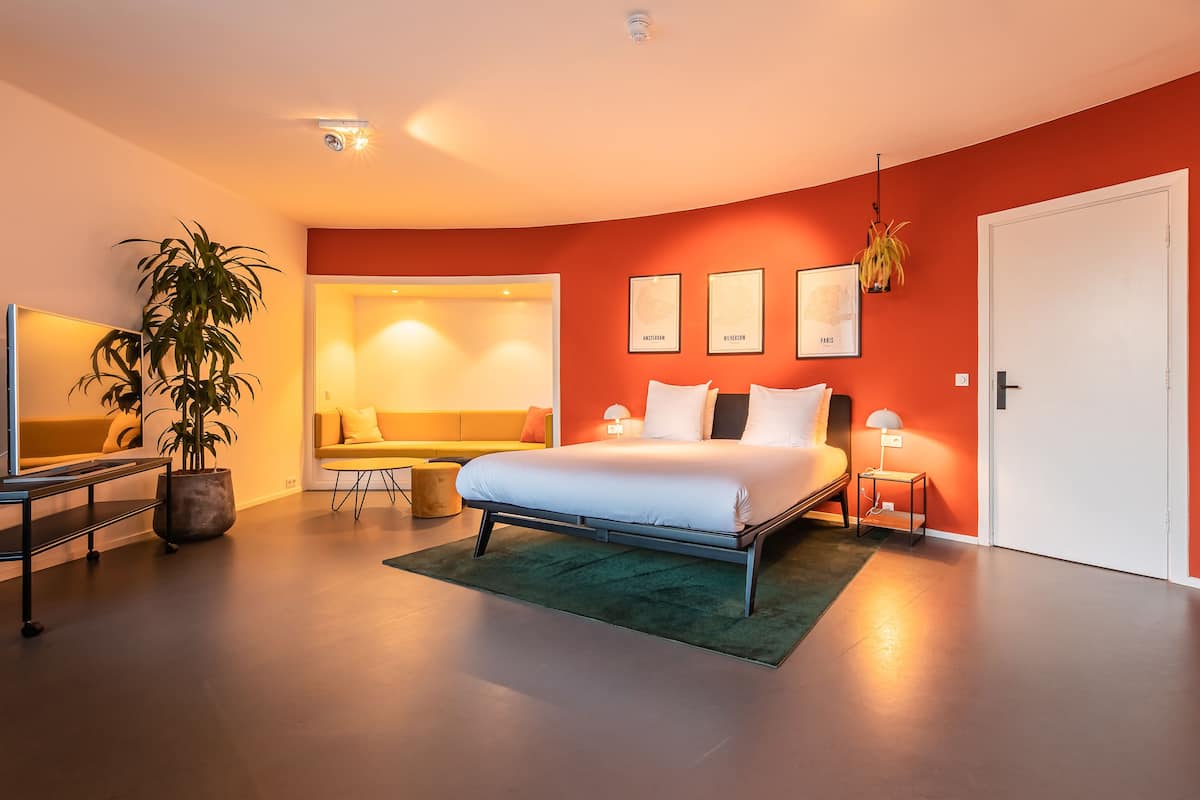 A modern bedroom with a bed, bedside tables, a sofa, and a large potted plant.